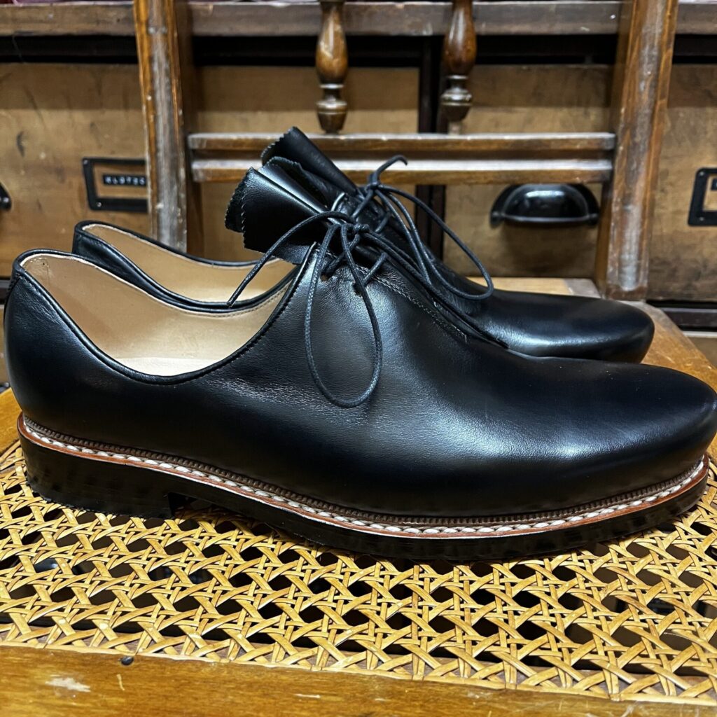 Schwarze Haferlschuhe mit Mittelschnürung auf einem Geflechtstuhl